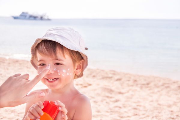 محافظت در برابر آفتاب دست مادر قفقازی در حال استفاده از کرم ضد آفتاب لوسیون برنزه از یک ظرف پلاستیکی به پسر شادش قبل از برنزه شدن در تعطیلات تابستانی در ساحل کپی اسپیس نزدیک
