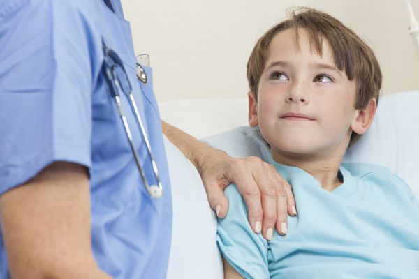 دکتر یا پرستار زن در حال دلداری از یک کودک پسر جوان در تخت بیمارستان