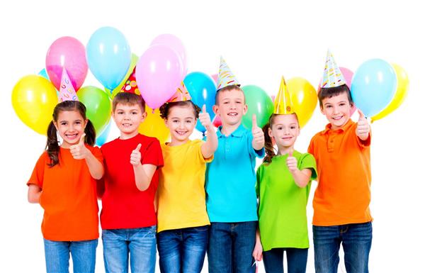 گروهی از کودکان شاد با تی‌شرت‌های رنگی و کلاه‌های مهمانی با بادکنک‌هایی که علامت شست را روی پس‌زمینه سفید نشان می‌دهند