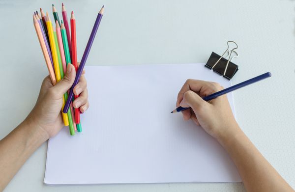 مردی که مشتی از مداد رنگی را در یک دست گرفته است در حالی که شروع به طراحی در یک کتاب طراحی می کند تا با دست دیگر خلاقیت و مهارت های هنری خود را به نمایش بگذارد نمایی از بالا
