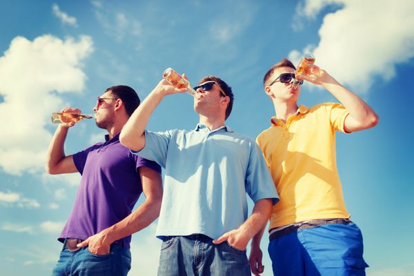 تابستان تعطیلات تعطیلات مفهوم افراد شاد - گروهی از دوستان مرد در حال تفریح در ساحل با بطری های آبجو یا نوشیدنی های غیر الکلی