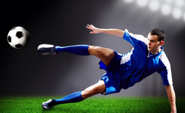 تصویر بازیکن فوتبال در حال انجام ضربه پروازی با توپ در زمین فوتبال