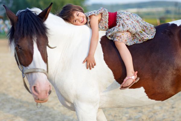 دختر کوچولو با لباسی که سوار بر اسب سفیدش می تازد