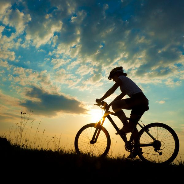 دختر دوچرخه سوار در غروب آفتاب در چمنزار