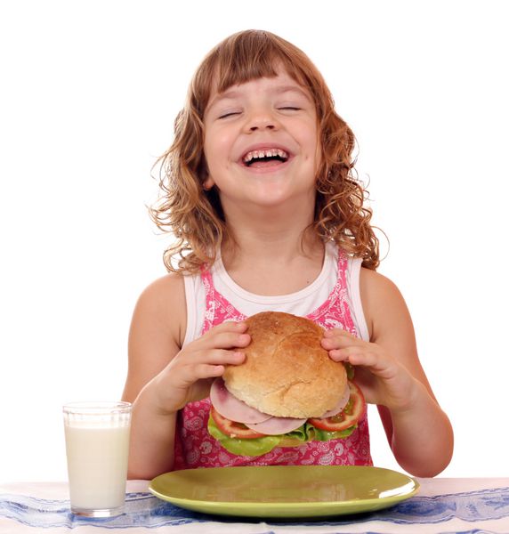 دختر کوچولوی شاد در زمان صبحانه ساندویچ بزرگ می خورد