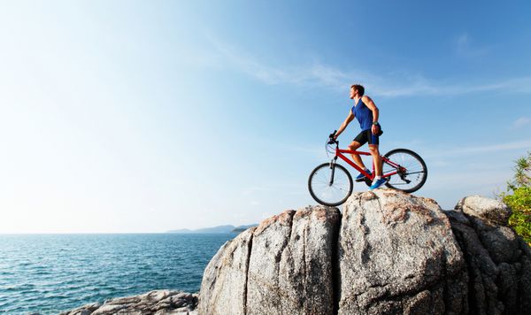 ورزشکار جوان با دوچرخه روی سنگ ایستاده است