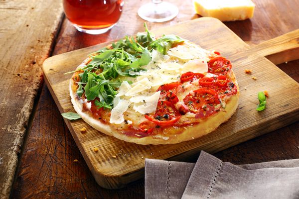 پیتزای رنگارنگ ایتالیایی در رنگ‌های ملی با برگ‌های سبز تازه راکت براده‌های سفید پنیر و گوجه‌فرنگی قرمز در سه راه راه که روی یک تخته چوبی روی یک میز قدیمی روستایی ایستاده است