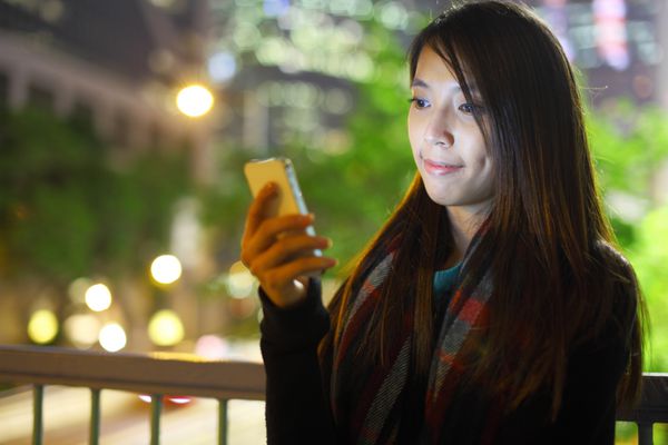 زن در شهر در شب از تلفن همراه استفاده می کند