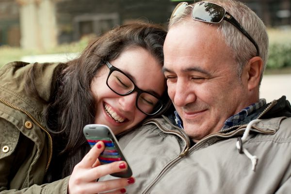 پدر و دختر نوجوان با سر در شانه در حال اشتراک گذاری چیزی خنده دار در تلفن همراه