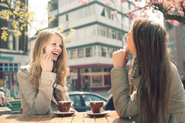 دو زن جوان در کافه بیرون از خانه صحبت می کنند و قهوه می نوشند