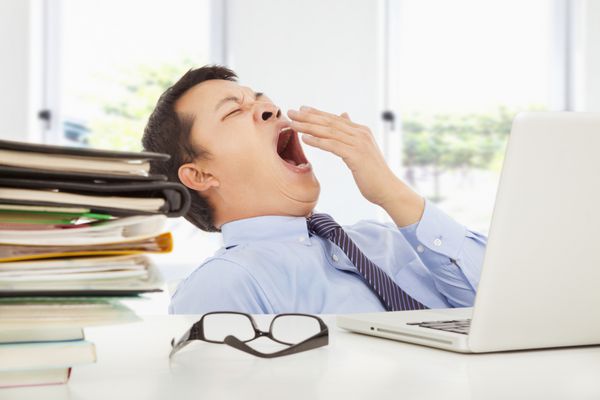 تاجر جوان خسته در محل کار در دفتر خمیازه می کشد