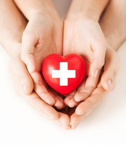 مفهوم سلامت خانواده خیریه و پزشکی - دستان مرد و زن که قلب قرمز را با علامت صلیب در دست دارند
