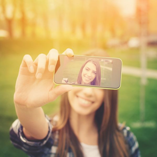زن جوان زیبا در حال عکاسی از خود با تلفن دختر نوجوان قفقازی خندان و ناز در حال گرفتن سلفی در فضای باز در روز آفتابی تابستان