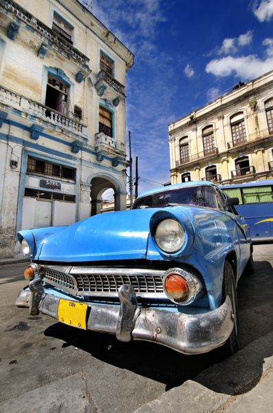 ماشین آبی کلاسیک آمریکایی در خیابان هاوانا با ساختمان‌های فرسوده در پس‌زمینه