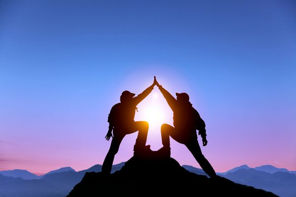سیلوئت دو مرد با ژست موفقیت که در بالای کوه ایستاده است