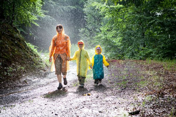 خانواده مادر پسر و دختر در حال قدم زدن در مسیری از جنگل در زیر باران