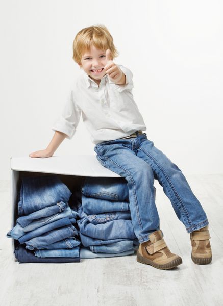 کودک روی جعبه مقوایی بسته بندی شده با شلوار جین نمایش شست بالا