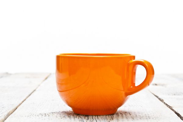 فنجان قهوه نارنجی روی میز چوبی