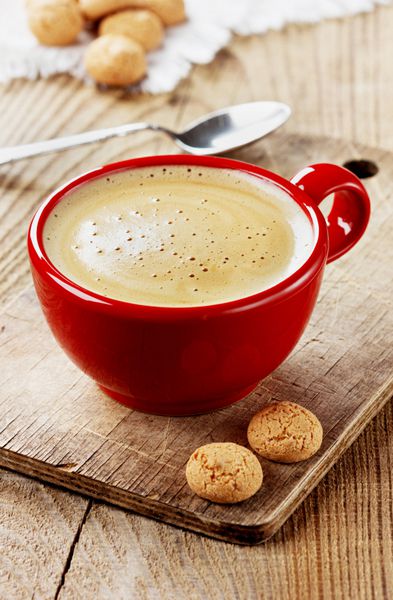 قهوه در یک فنجان قرمز با کلوچه های بیسکویت روی یک تخته چوبی روستایی