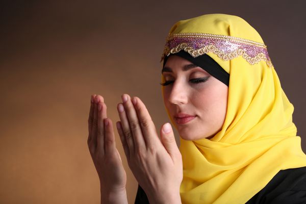 زن زیبای عربی مسلمان در حال نماز در زمینه رنگ تیره