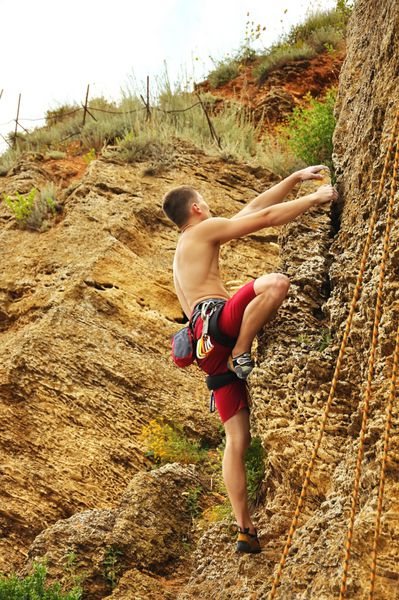 کوهنورد عضلانی جوان در حال بالا رفتن از دیوار صخره ای