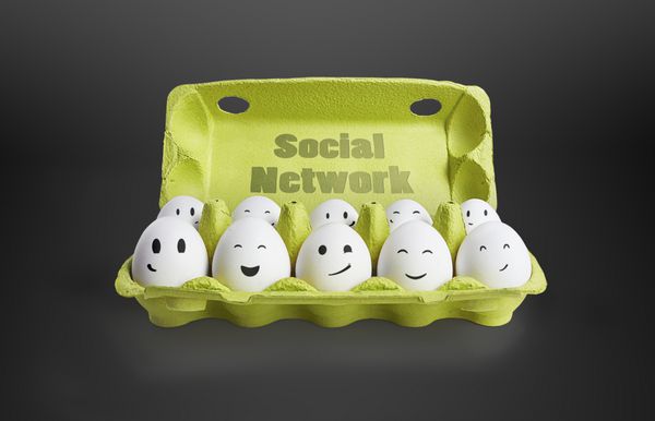 گروهی از تخم مرغ های شاد با چهره های خندان که نشان دهنده یک شبکه اجتماعی است ده تخم مرغ سفید در یک جعبه کارتن در زمینه مشکی