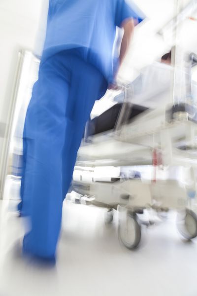 عکسی با حرکت تار از یک بیمار روی برانکارد یا تخت خواب که با سرعت از طریق راهروی بیمارستان توسط پزشکان پرستار به اتاق اورژانس هل داده می‌شود