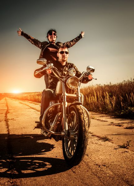زوج دوچرخه سوار با ژاکت چرمی که سوار بر موتورسیکلت در جاده هستند