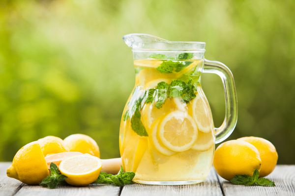 تهیه نوشیدنی لیموناد لیموناد در کوزه و لیمو با نعنا روی میز در فضای باز