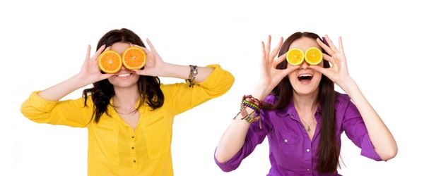 دو دختر شاد در زمینه سفید دو دختر یک مرکبات را در دستان خود نگه می دارند چشم لیمو و پرتقال را ببندید شاد لبخند سلامتی شادی میوه های تازه - مردم سبک زندگی سالم