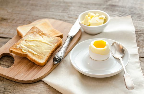 تخم مرغ آب پز با نان تست ترد روی میز چوبی