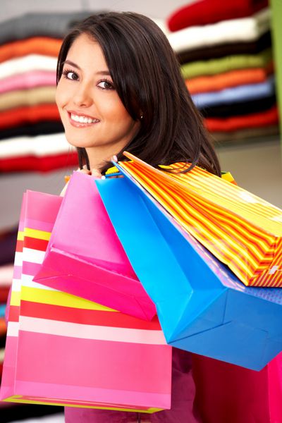 دختری در یک فروشگاه خرده فروشی لبخند می زند و کیف های خرید را حمل می کند