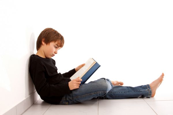 Junge liest am Boden sitzend konzentriert ein Buch