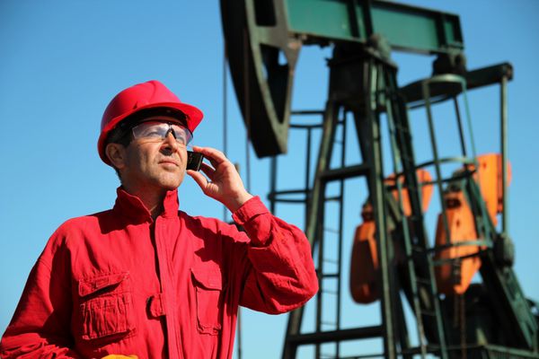کارگر نفت با استفاده از تلفن همراه در کنار Pumpjack