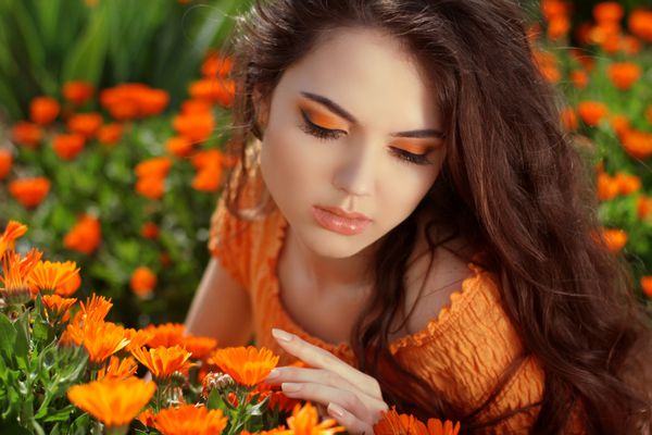 پرتره زن جوان در فضای باز بر روی گل های گل همیشه بهار نارنجی
