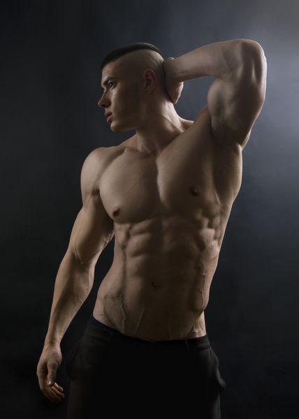 مرد جوان با بدنی ورزشی که روی پس زمینه سیاه ژست گرفته است