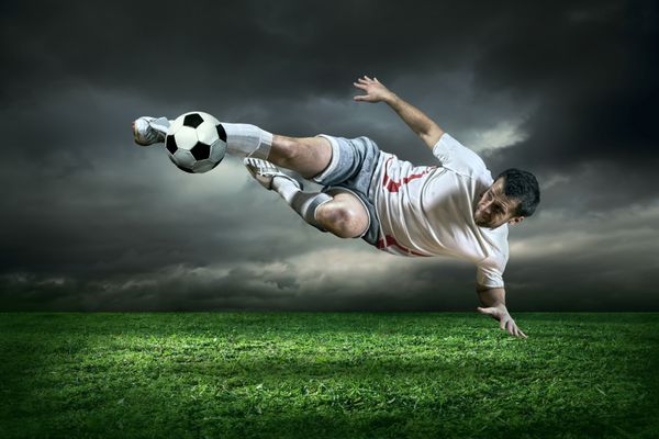 بازیکن فوتبال با توپ در حال عمل زیر باران در فضای باز