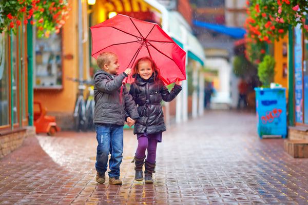 بچه های شادی که زیر باران در خیابان رنگارنگ راه می روند