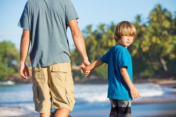 پدر و پسر شادی که با هم در ساحل قدم می زنند بی خیال