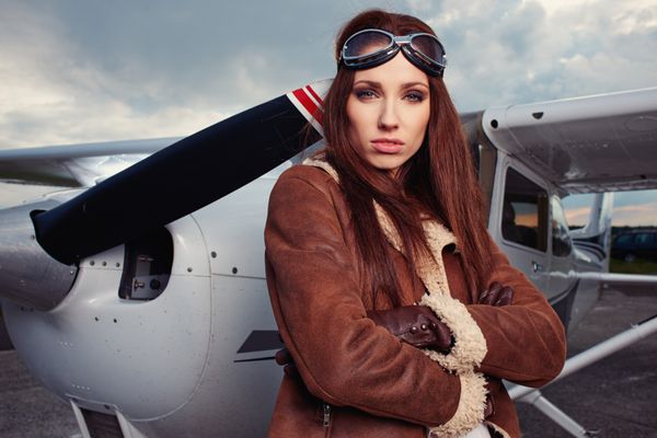 پرتره زن جوان زیبا خلبان در مقابل هواپیما