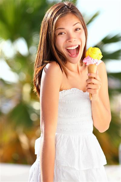 دختر بستنی با هیجان و خوشحالی از خوردن بستنی مخروطی در ساحل در تعطیلات تابستانی زن جوان قفقازی چینی آسیایی دوست داشتنی در خارج از خانه