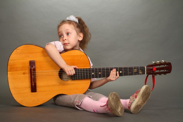 دختر کوچک با یک گیتار بزرگ روی زمین نشسته است نگاهی که در لنز نیست یک دوبل 2