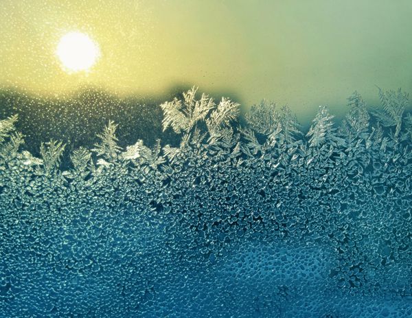 الگوی طبیعی یخ زده و آفتاب روی شیشه زمستانی