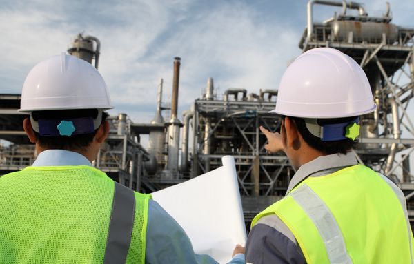 دو مهندس صنعت نفت در حال بحث درباره یک پروژه جدید با پیشینه بزرگ پالایشگاه نفت هستند