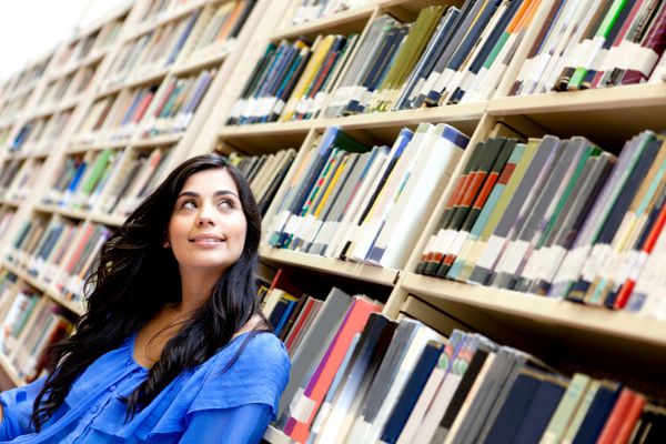 زن متفکر در کتابخانه احاطه شده توسط کتاب