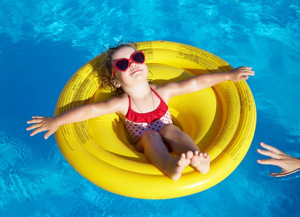 دختر کوچولوی بامزه در یک حفاظ زرد رنگ در یک استخر شنا می کند