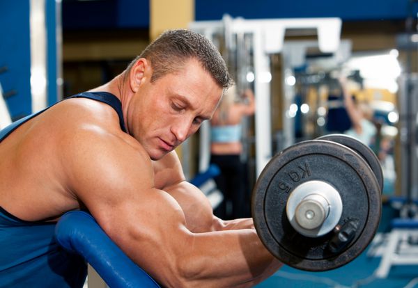 مرد با تجهیزات تمرین وزنه در باشگاه ورزشی