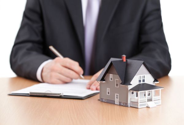 مفهوم املاک و مستغلات - تاجر در پشت مدل معماری خانه قرارداد امضا می کند