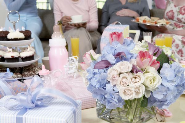دسته گل و هدایایی روی میز با زنان در پس زمینه در حمام نوزاد