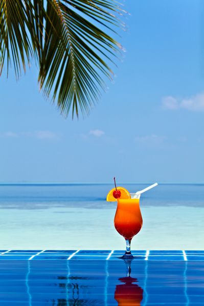 لیوان آب پرتقال در لبه استخر ساخته شده از کاشی لعابدار در ال استوایی مالدیو است